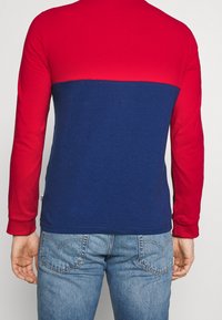 Maglietta a maniche lunghe con maniche rosse e corpo blu, realizzata in cotone con una texture liscia. Design colorblock notevole nella parte posteriore.