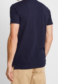 Námořnická modrá polo tričko, krátké rukávy, měkký bavlněný materiál, postranní rozparky na lemu, rovný střih, minimalistický design, žádné viditelné značky.