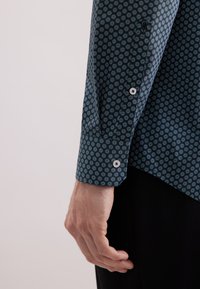 Camicia a maniche lunghe in tessuto blu scuro con motivi circolari in blu chiaro. Presenta polsini con bottoni e una vestibilità sagomata.