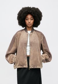 Καφέ μπουφάν μπόμβερ από κοτλέ ύφασμα με ραβδωτή υφή, ελαστικά μανίκια και φερμουάρ στο μπροστινό μέρος. Διαθέτει σκούρες καφέ ραβδώσεις αντίθεσης στους ώμους.