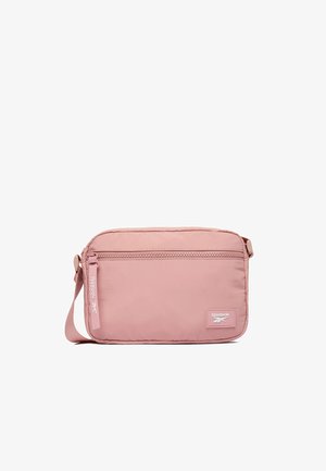 Pequeño bolso bandolera rectangular rosa de Reebok con bolsillo frontal con cremallera, correa ajustable y parche con el logo en la esquina inferior derecha.