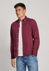 Bordeaux knoopshirt met een kraag, lange mouwen en een rechte zoom. Draag het over een wit T-shirt met een relaxte pasvorm en spijkerbroek.