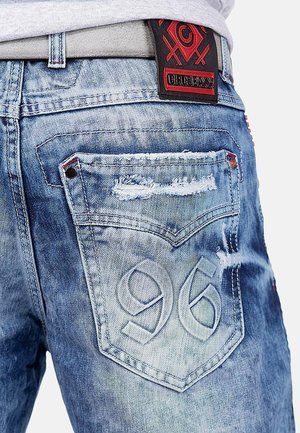 Faded blue denim jeans with distressed details, contrasting stitching, and a textured black and red leather patch on the waistband.