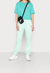 Camiseta corta de color verde menta con un logo, combinada con pantalones jogger a juego en verde menta y zapatillas blancas. Bolsa negra de bandolera con logo.
