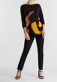 Svart stickad tröja med abstrakta gula och bruna mönster, båt-ringning och långa ärmar, ihop med åtsittande svarta byxor och svarta klackar.