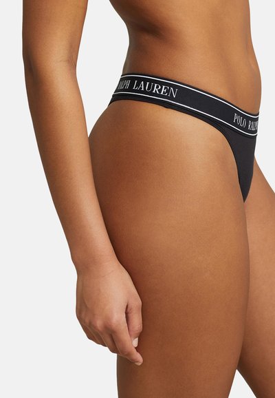 Melnā string veida apakšveļa ar auduma joslu, uz kuras ir baltais "Polo Ralph Lauren" logo. Gluda tekstūra un minimālisma dizains.