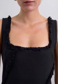 Zwarte kleding met een vierkante halslijn, met rafelige accenten langs de randen en een gladde textuur. Close-up van de stof.