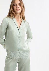 Zestaw satynowych piżam w delikatnej zieleni, z kołnierzykiem, zapinany na guziki z przodu oraz subtelną koronką przy brzegu. Gładka faktura i luźny krój.