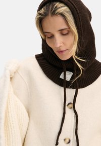 Kremowa kurtka z mieszanki wełny z brązowym dzianinowym kapturem, zapinana na guziki, z prążkowanymi detalami na rękawach. Teksturowana tkanina z kontrastującymi kolorami.