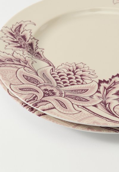 Pile d'assiettes en céramique couleur crème avec des motifs complexes de fleurs et de feuilles violettes le long des bords sur un fond blanc.