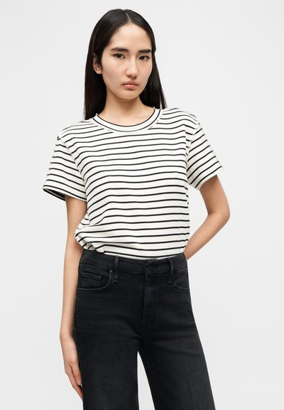 Μαύρο και άσπρο ριγέ T-shirt με στρογγυλή λαιμόκοψη και κοντά μανίκια, συνδυασμένο με ψηλόμεσα μαύρα τζιν. Ομαλή υφή υφάσματος.