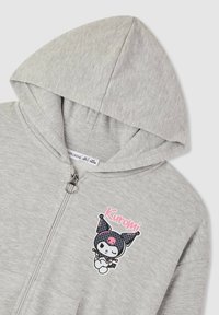 Felpa con zip grigia chiara e cappuccio, con un piccolo personaggio dei cartoni animati "Kuromi" in nero e rosa sul petto.