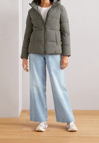 Oliveenvihreä toppatakki, jossa vetoketjullinen etuosa, kiinnitetty huppu ja tikattu malli. Yhdistetty leveälahkeisiin vaaleansinisiiin farkkuihin ja monivärisiin lenkkareihin.