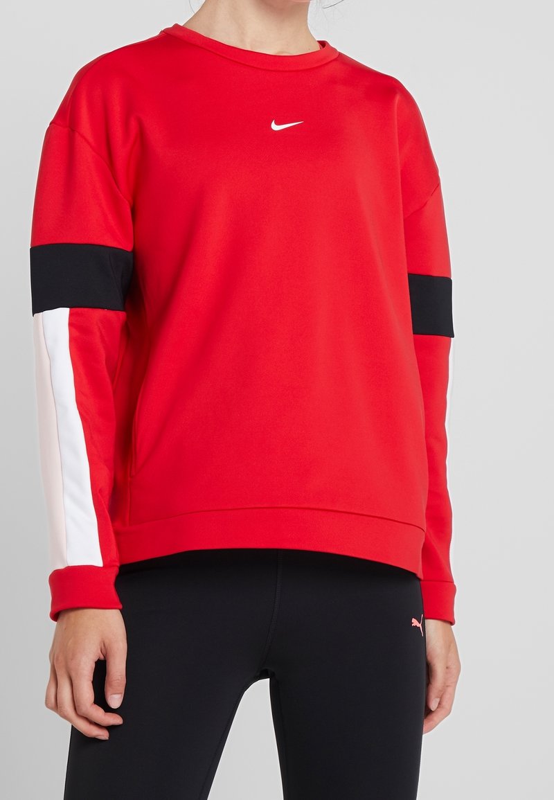 Personne portant un sweat-shirt rouge Nike avec des bandes noires et blanches sur les manches et un legging noir Puma.
