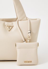Sac à main beige Guess avec une petite pochette attachée, les deux présentant des accents en logo doré et une texture en cuir lisse.