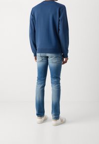 Granatowa bluza z żebrowanymi mankietami i ściągaczem, zestawiona z jasnoniebieskimi, dopasowanymi dżinsami o wyblakłym wyglądzie i detalami na tylnej kieszeni.