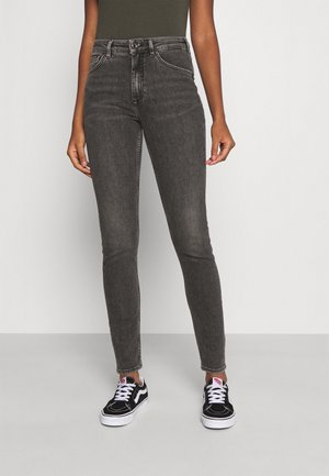 Jeans ajustados en denim gris oscuro, de cintura alta y con un acabado desgastado. Combinados con zapatillas negras con suelas y cordones blancos.
