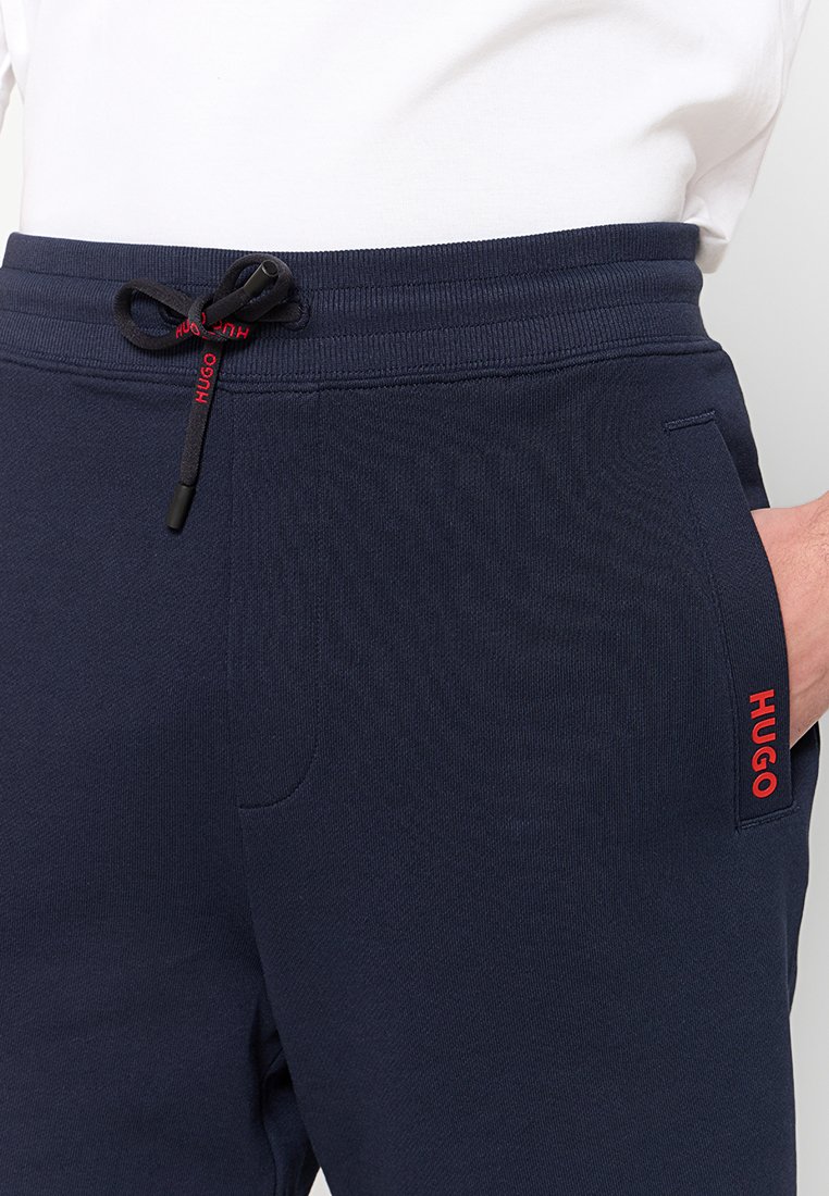 Nautisch blaue Sweatpants aus einem strukturierten Material, mit elastischem Bund und Kordelzug. Verfügt über eine Seitentasche und ein rotes "HUGO"-Logo auf dem Oberschenkel.