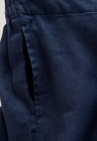 Gros plan sur un tissu bleu foncé avec une texture visible et une couture verticale, montrant l'ouverture d'une poche latérale.