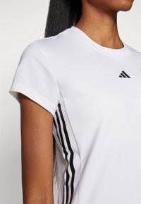 Valge spordit-särk lühikeste varrukatega, mille külgedel on kolm musta vertikaalset triipu ja ülemisel rinnaosal adidas logo.