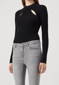 Top negro de manga larga acanalado con un diseño cortado, combinado con jeans ajustados grises. La tela parece suave y texturizada. Acento de anillo plateado en la mano.