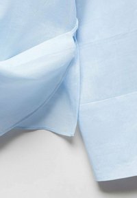 Camicia azzurro chiaro realizzata in un tessuto morbido, con taglio dritto, spacco laterale e cuciture rifinite con cura.