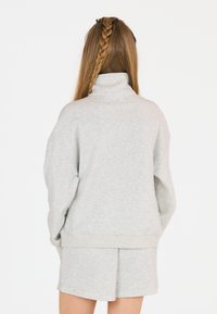 Hellgrauer Sweater mit hohem Kragen und überschnittenen Schultern, kombiniert mit passenden Shorts. Weicher Baumwollmix und lockere Passform.