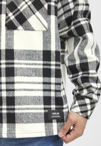 Camicia flanella a quadri bianca e nera con taschino sul petto, tessuto texturizzato e etichetta all'orlo. Maniche lunghe con dettagli sui polsini.