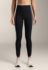 Black high-waisted leggings with white side stripes, made of smooth, stretch fabric. Features a fitted design and ankle-length cut.