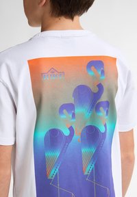 Hvid bomulds T-shirt med et farverigt grafisk print af stiliserede flamingoer i en blå, lilla og orange gradient på ryggen.