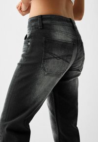 Svarta denimjeans med ett urtvättat mönster, med en bakficka med X-sömdesign och en klassisk midja.