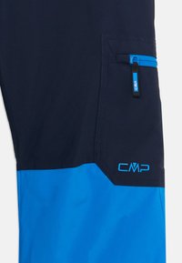 Sötétkék és világoskék túranadrág cipzáras zsebbel és CMP logóval. A anyag simának tűnik; a kontrasztos színpanelok fokozzák a vizuális részleteket.