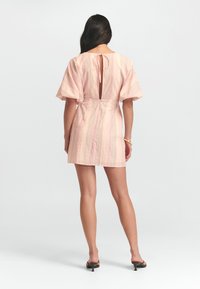 Vestido corto rosa con mangas anchas, abertura en la parte posterior con forma de llavero, sutiles rayas verticales y una textura suave. Combinado con unos tacones de tipo fácil de poner.