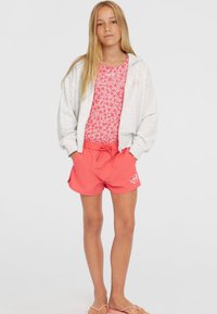 Grå zip-up hoodie over en pink blomster badedragt, parret med koralfarvede shorts. Skoene er lyse pink flip-flops. Enkel design med snøre.