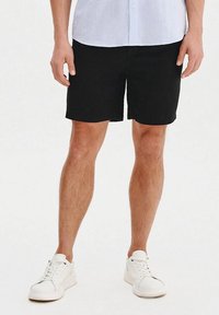 Czarne szorty wykonane z lekkiego materiału, proste, z p�łaskim przodem, noszone z białymi trampkami i jasnoniebieską koszulą z guzikami.