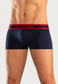 Boxers bleu marine avec une ceinture élastique rouge et noire griffée, offrant une coupe ajustée et une texture lisse, conçus pour le confort et le maintien.