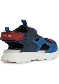 Sandal navy y rojo con parte superior de malla, correas ajustables y suela de goma blanca. Presenta cortes para ventilación y una etiqueta en el talón con la marca.