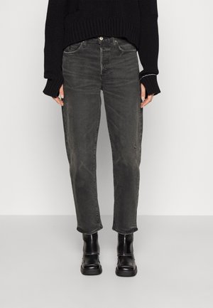 Osoba nosząca wyblakłe czarne proste jeansy, czarny dziany sweter z długimi rękawami i czarne botki do kostki z białym przeszyciem.