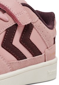 Różowe sneakersy z teksturowaną cholewką ze skóry, ciemnoróżowymi akcentami w zygzak, rzepem oraz białą gumową podeszwą.