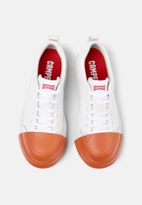 Zapatillas blancas con una puntera de goma naranja, diseño con cordones, cuerpo de cuero texturizado y forro interior rojo que presenta el logo "CAMPER".