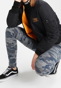 Vans bomberjacka i svart med orange foder, grå kamouflageleggings och svarta sneakers. Har en zipficka och vita sulaaccenter.