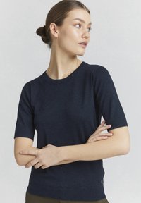 Navy short-sleeve knitted sweater with ribbed neckline and cuffs. Soft texture. Fitted design with a small branded detail at the hem.