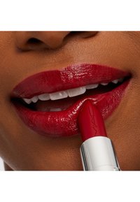 Red lipstick being applied to full, glossy lips with a smooth texture. The lipstick has a silver, branded casing.
