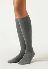 Graue knielange Socken aus weichem, strukturiertem Stoff mit einem gerippten Bündchen. Glatter Zehenbereich und minimales Muster überall.
