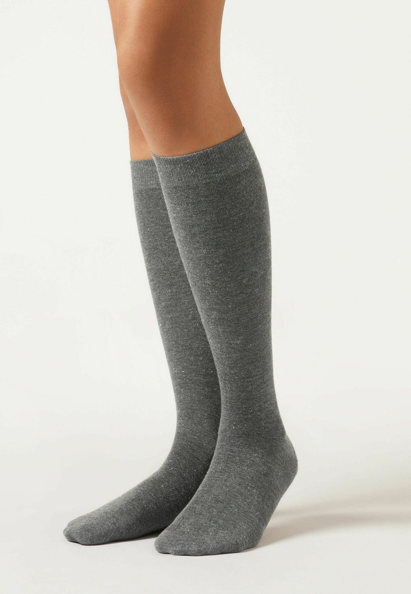 Graue knielange Socken aus weichem, strukturiertem Stoff mit einem gerippten Bündchen. Glatter Zehenbereich und minimales Muster überall.