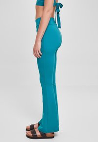 Pantaloni yoga a zampa d'elefante color verde acqua, realizzati in tessuto elasticizzato, con una vita alta. Il modello indossa sandali con platform neri. Texture morbida, vestibilità aderente.