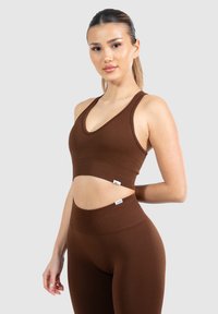 Sujetador deportivo marrón con canalé y un profundo escote en V, combinado con leggings de talle alto a juego que poseen una cinturilla sin costuras.