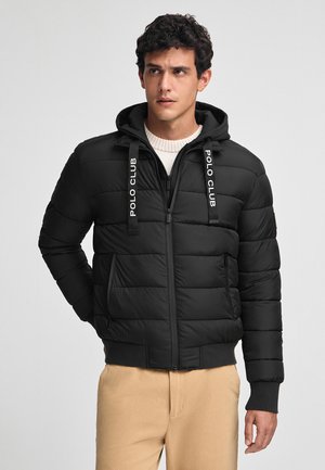 Giacca a vento nera con cappuccio, caratterizzata da una texture trapuntata, con il contrastante marchio bianco "POLO CLUB" sui cordini e chiusura con zip.