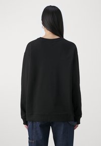 Zwarte sweatshirt met een ronde halslijn en lange mouwen, met een relaxte pasvorm en een gladde textuur, gedragen over blauwe jeans.