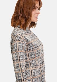 Langemouwen top in geweven stof met een ruitpatroon in zwart, wit en roestkleuren; hoge halslijn en rechte silhoët.